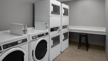 Una sala de lavandería con lavadoras y secadoras apiladas, un taburete pequeño y una encimera blanca.