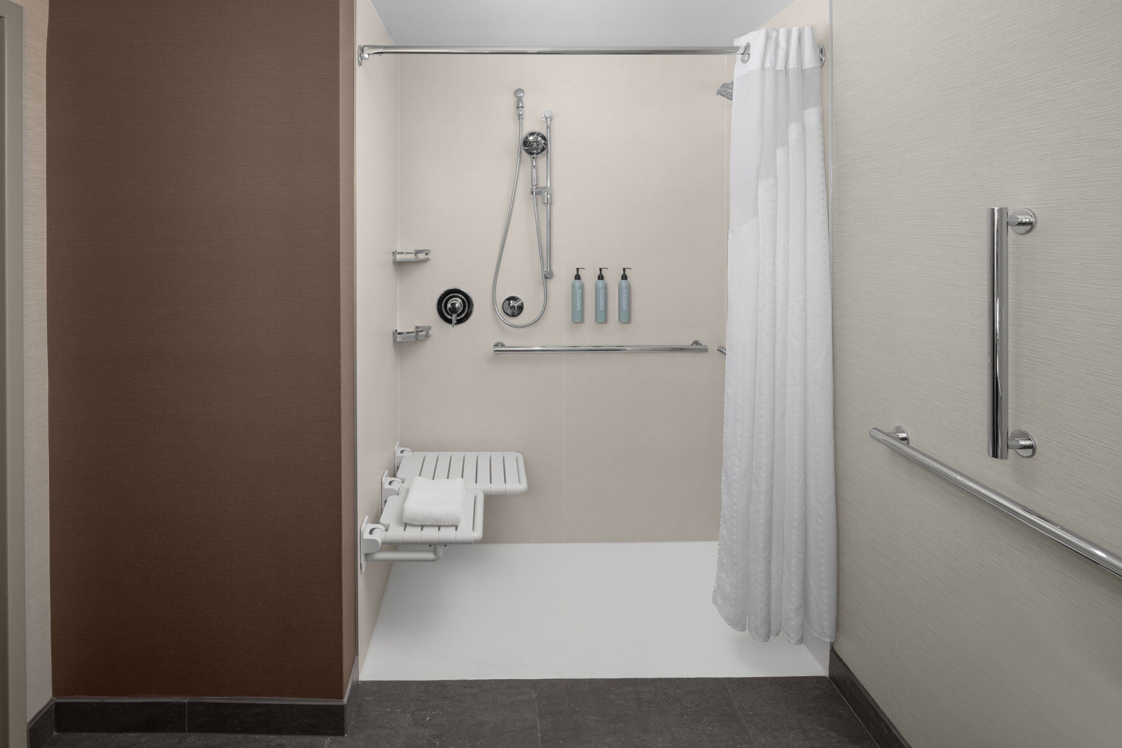 A modern bathroom with a shower, grab bars, a towel rack, and a toilet.