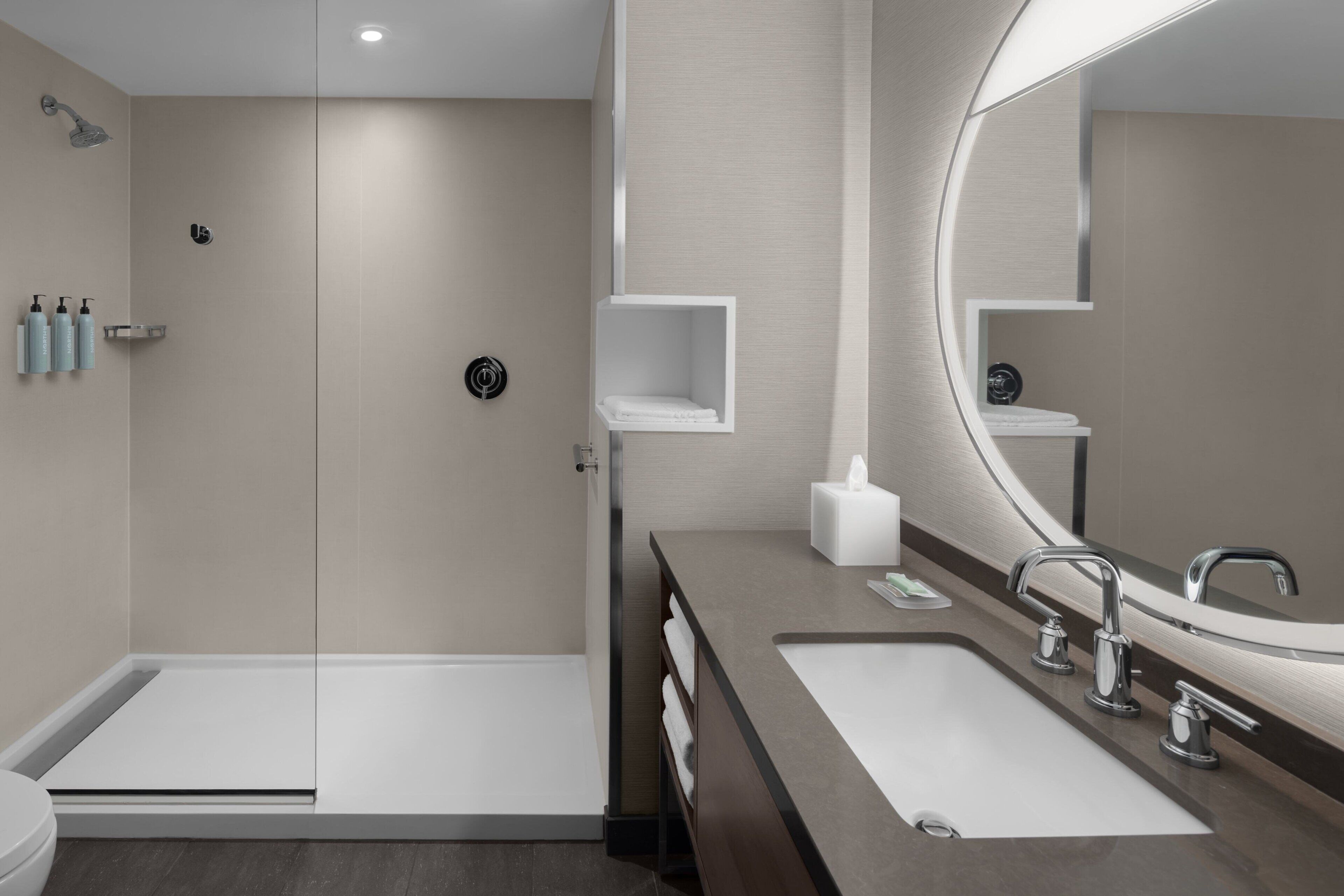 Un baño moderno con cabina de ducha de vidrio, tocador doble y un espejo grande.