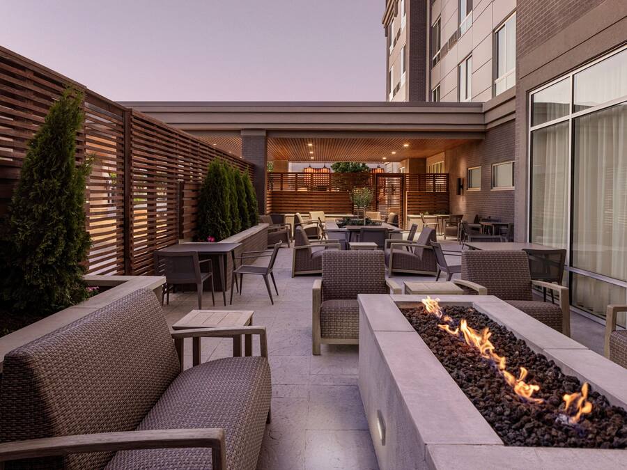 Un patio al aire libre con mobiliario, una chimenea y un edificio moderno al fondo.