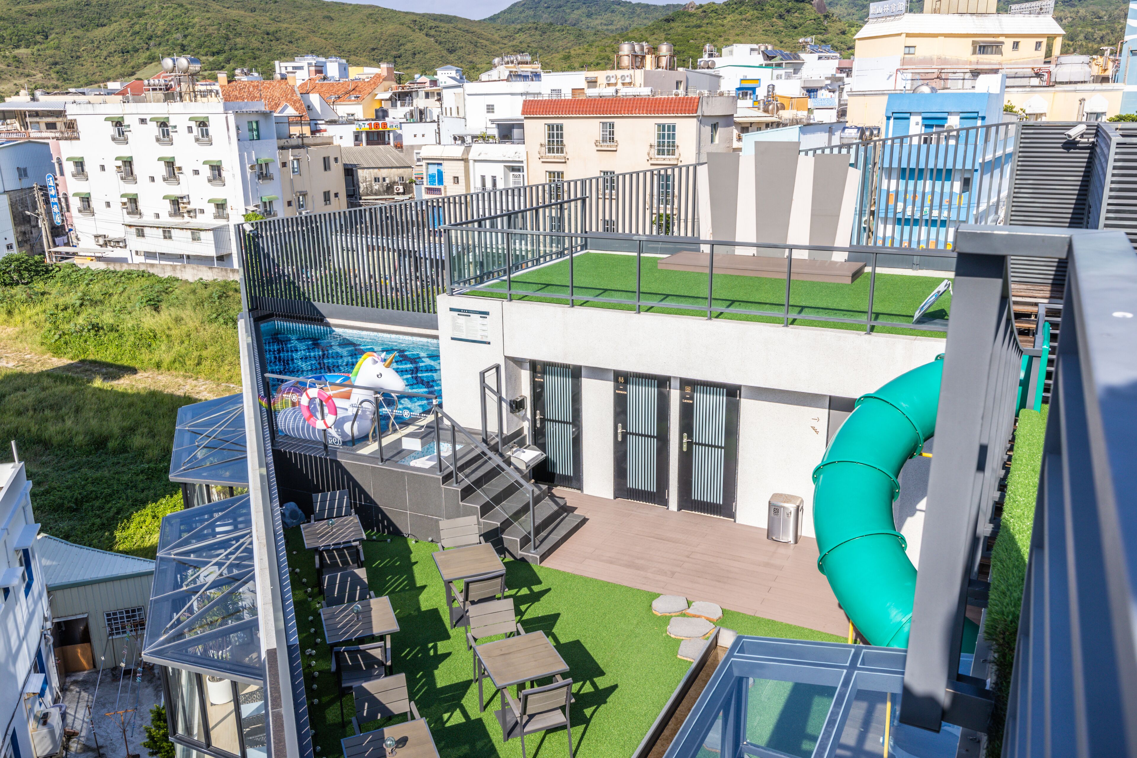 A rooftop pool area with a slide, outdoor seating, and a view of the surrounding buildings.