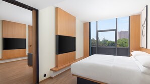 A modern hotel room with a large bed, built-in TV, and a large window offering a city view.