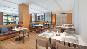 A modern restaurant with high tables and booths, large windows, and a wooden floor.