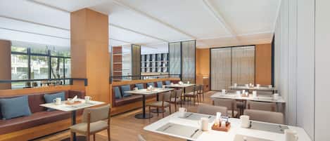 Un restaurante moderno con mesas altas, cabinas, ventanas amplias y suelo de madera.