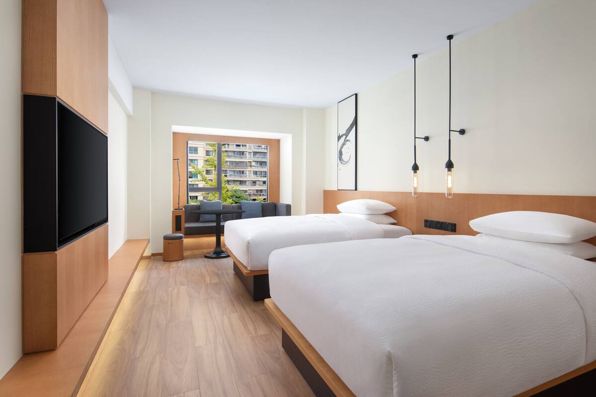 Een moderne hotelkamer met twee bedden, een flatscreen televisie, een zithoekje en een raam met uitzicht op een gebouw.