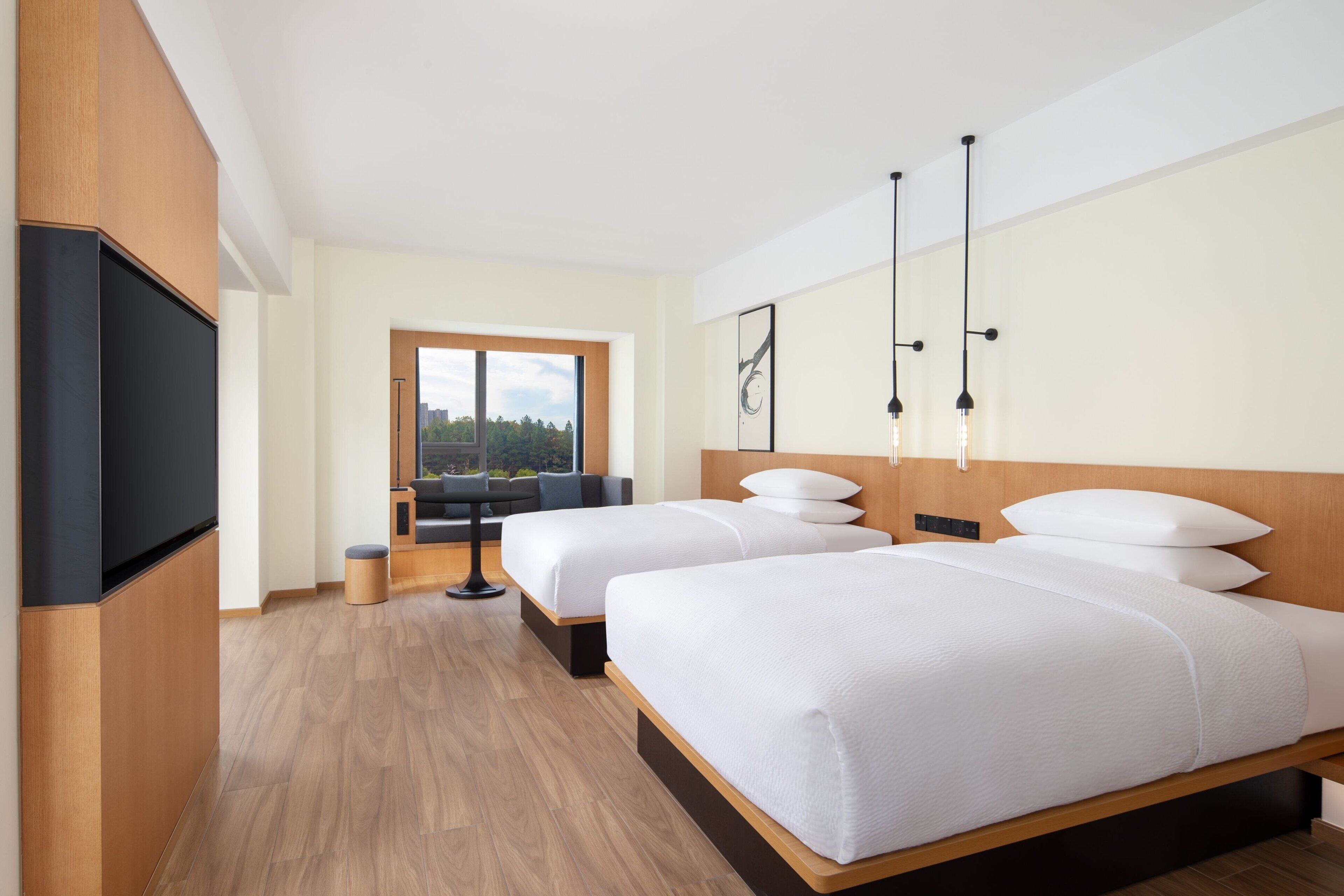 Moderni hotellihuone, jossa on kaksi sänkyä, televisio, suuri ikkuna ja näkymä ulos.