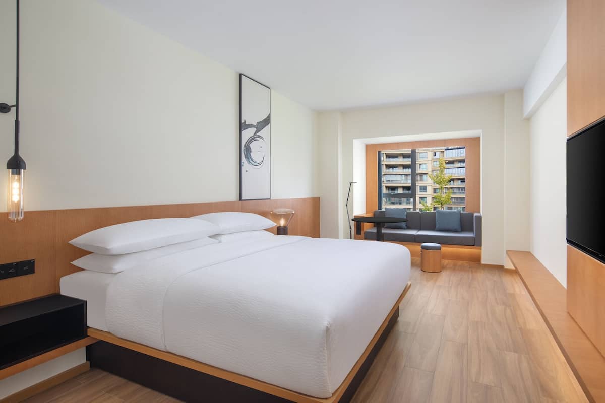 Een moderne hotelkamer met een groot bed, een televisie, een bank en uitzicht op de stad.