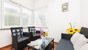 Une pièce comprenant deux fauteuils en osier, une table basse en verre, un canapé et un vase avec des fleurs.