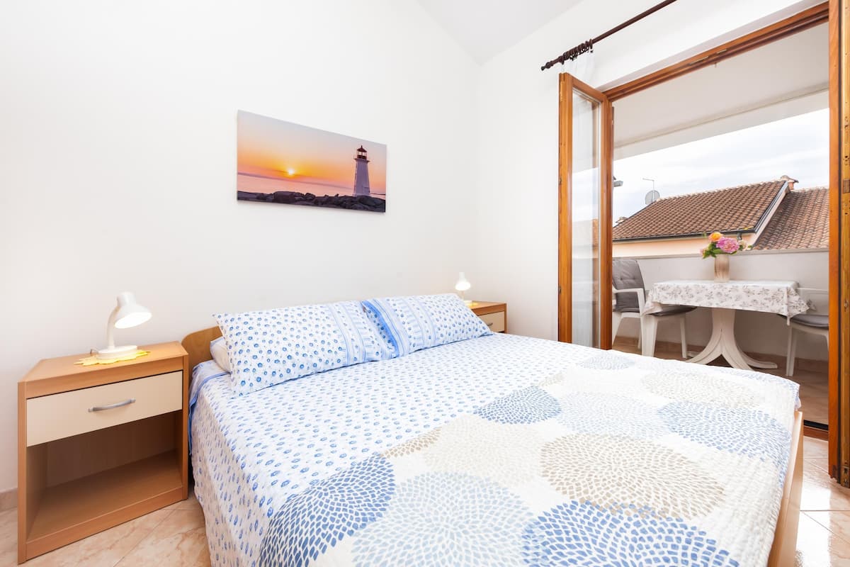 A bedroom with a bed, nightstand, and a painting of a lighthouse.
