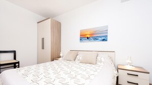 Une chambre à coucher comprenant un lit, des tables de chevet, une armoire et un tableau représentant un coucher de soleil sur l’océan, accroché au mur.