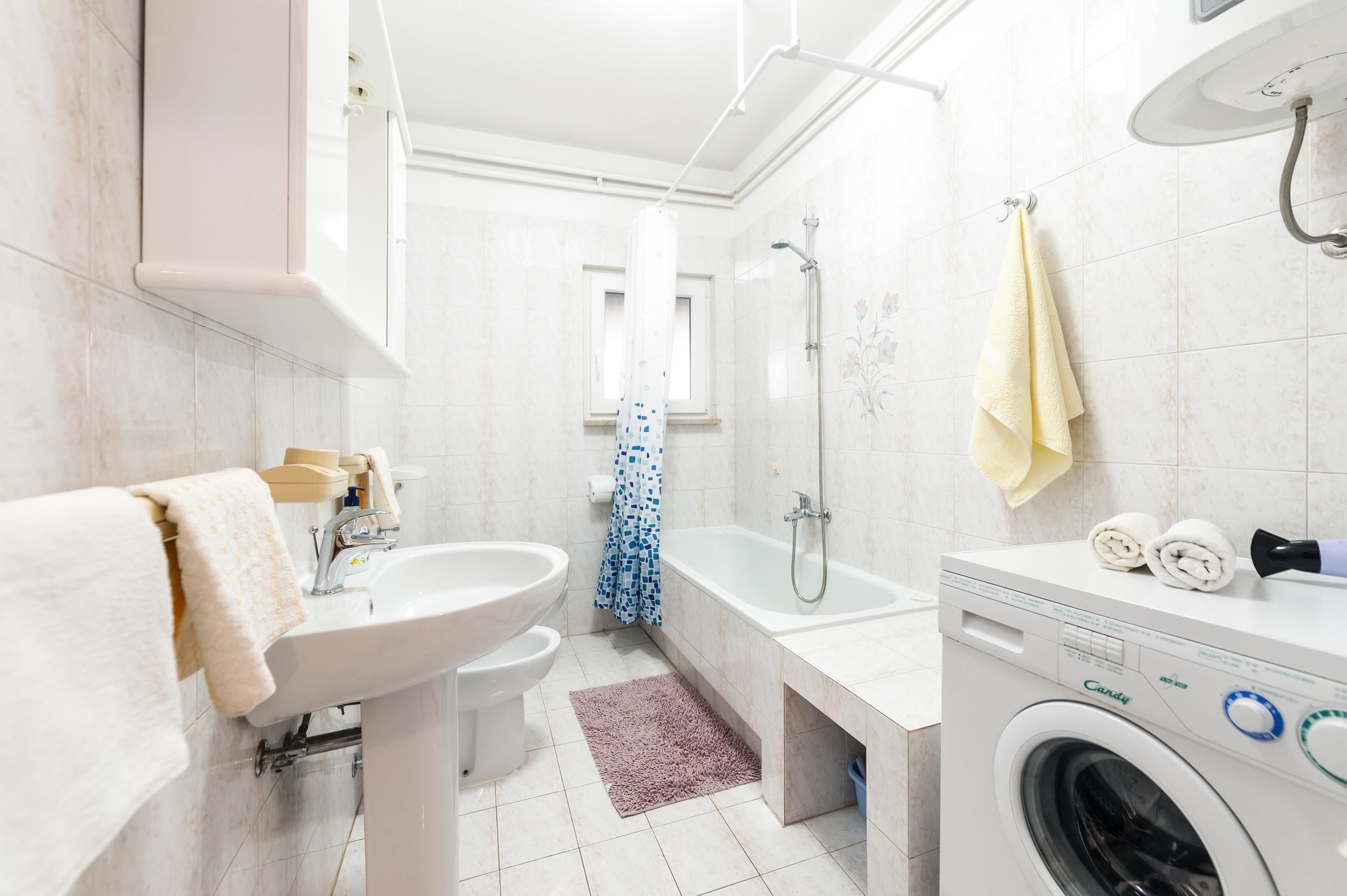 A modern bathroom with a sink, toilet, bathtub, and a front-loading washing machine.