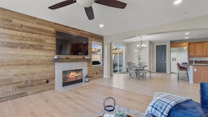 A spacious living area with a fireplace, a ceiling fan, and a modern kitchen in the background. - Resort-style Home with stunning views, pool, hot tub, putting green (Fallbrook)