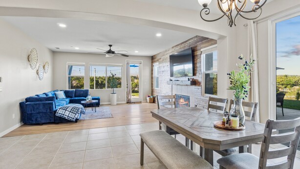 A spacious living area with a blue sofa set, a dining table with chairs, a fireplace, and a large window offering a view of the outdoors. - Resort-style Home with stunning views, pool, hot tub, putting green (Fallbrook)