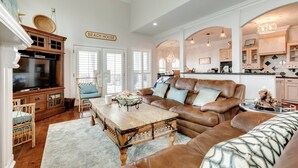 A spacious living room with a brown leather sofa, a wooden coffee table, wicker chairs, and a television.