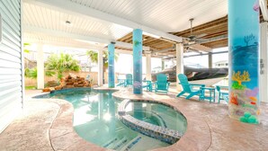 A covered swimming pool area with a stone deck, blue chairs, and a mural on a pillar.