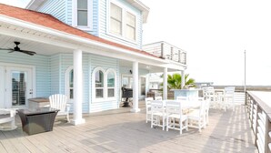 A coastal house with a covered deck, outdoor furniture, and a view of the ocean.