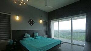 A modern bedroom with a large bed, a ceiling fan, and a city view through a large window.