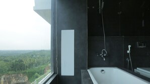 A modern bathroom with a large bathtub and a shower, a window with a view of a forested area, and a dark wall.