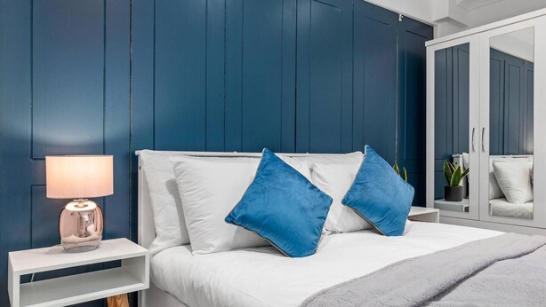 Ein Schlafzimmer mit einem weißen Bett, blauen Kissen, einer Nachttischlampe und einem Kleiderschrank.