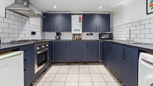 Eine moderne Küche mit dunkelblauen Schränken, einer weißen Fliesenfassade, Edelstahlgeräten und Einbauleuchten.