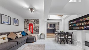 Ein modernes Wohnzimmer mit einem grauen Sofa, einer roten Telefonzelle und einem Essbereich mit einem Fernseher, der Filmplakate zeigt.