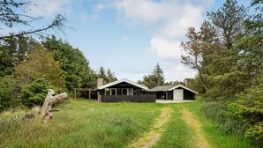 Una casa moderna con un ampio garage e una zona esterna coperta, immersa in una fitta foresta.