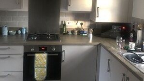 A modern kitchen with a gas stove, oven, and stainless steel cabinets. There is a digital clock on the oven and a wine glass on the counter. - Impeccable 2-bed House in Attleborough (Attleborough)