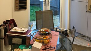 A dining area with a glass table, chairs, and a red and white checkered tablecloth. There is a basket with fruits and a bottle on the table. - Impeccable 2-bed House in Attleborough (Attleborough)