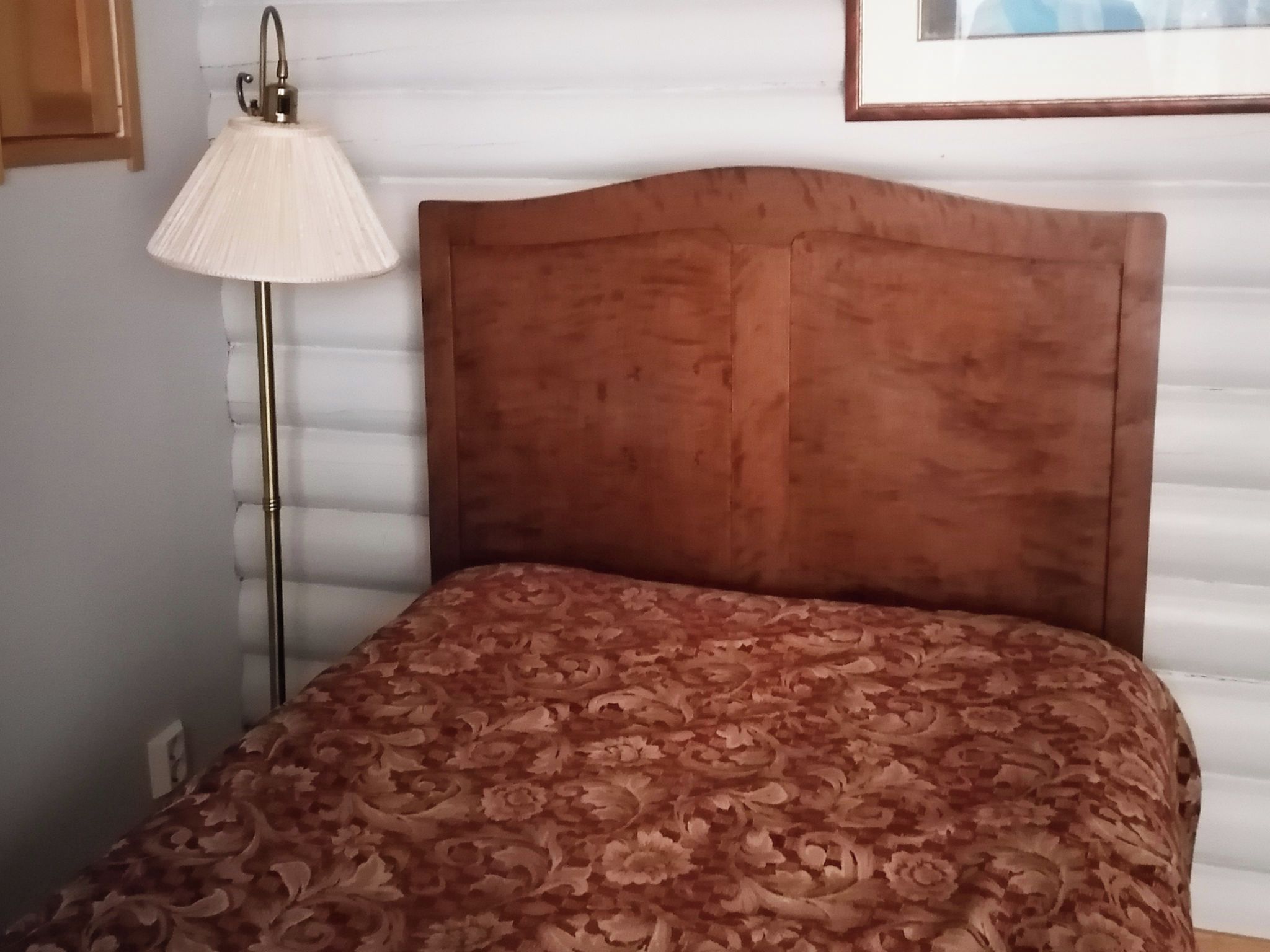 Una cama con una colcha estampada, una lámpara de noche y un cuadro en la pared.