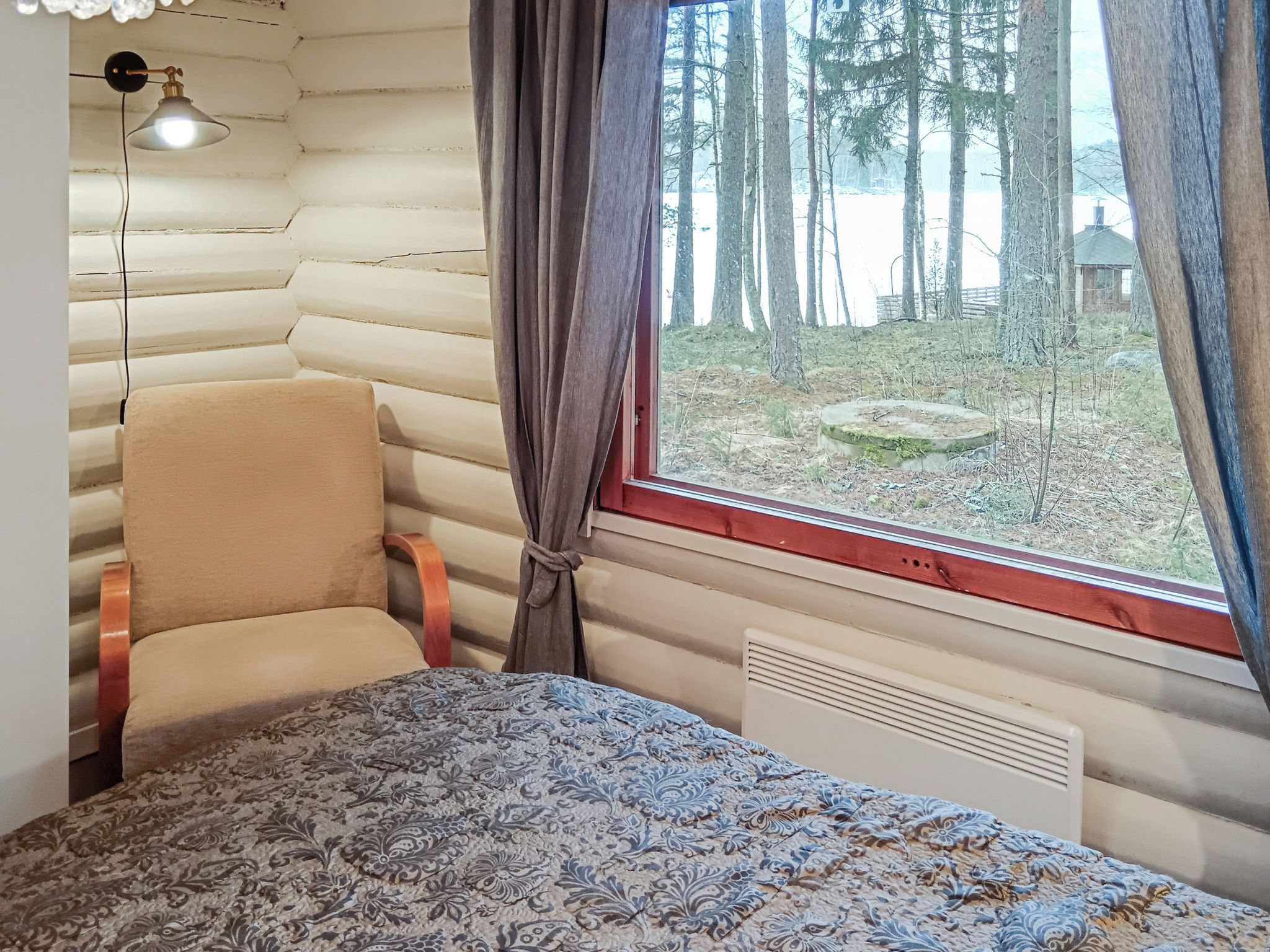 A room with a bed, a chair, a window with curtains, and a lamp.