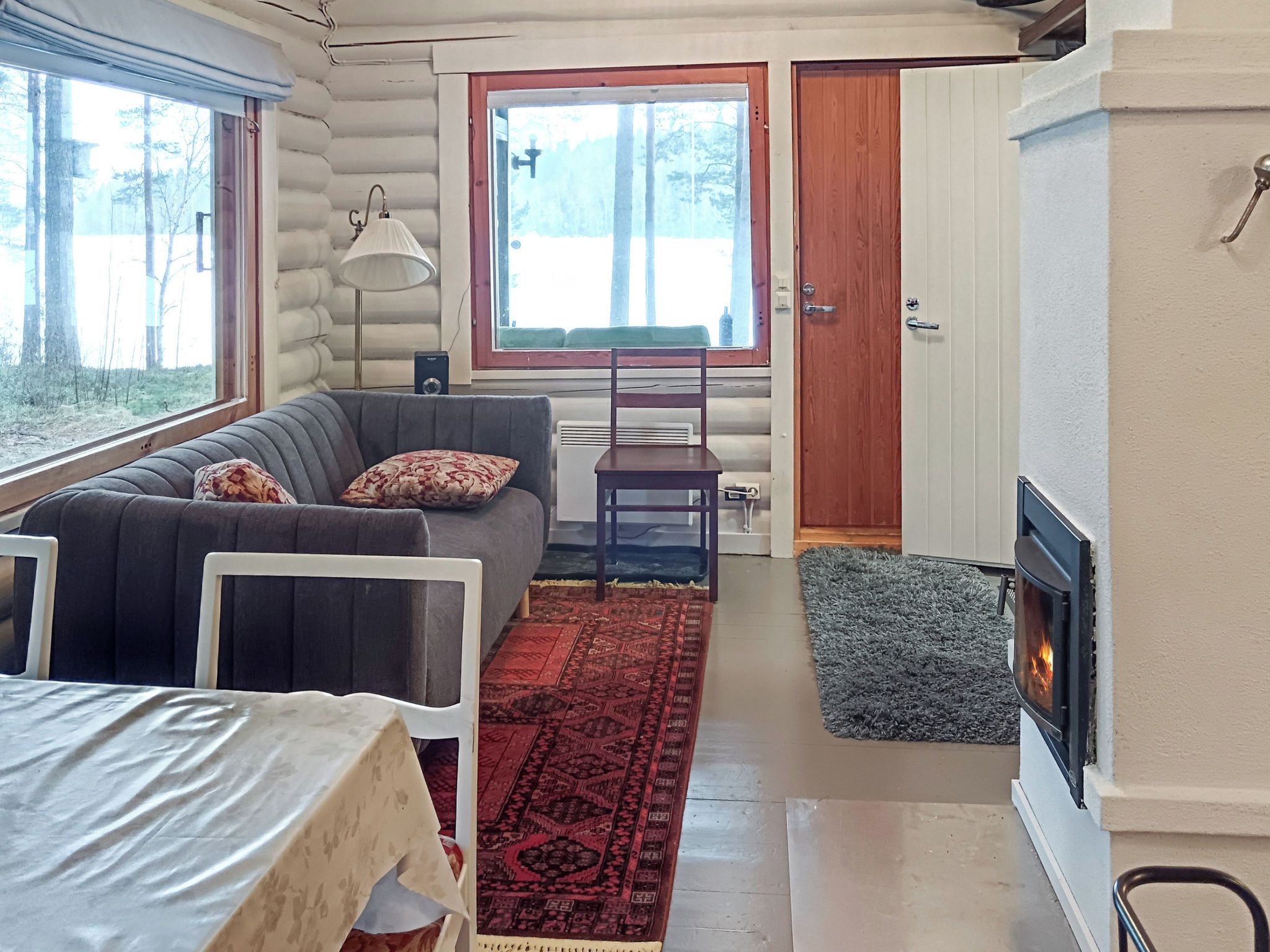 En mysig stuga med en soffa, ett matbord, en öppen spis och ett stort fönster.
