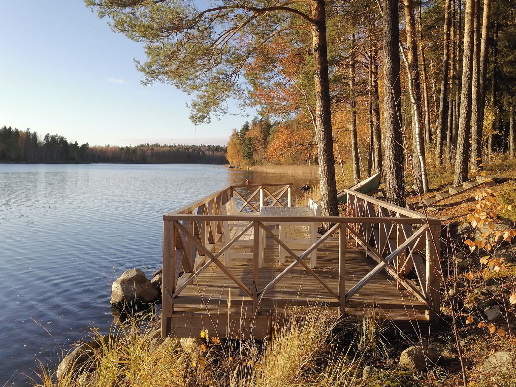 Un muelle de madera se adentra en un lago tranquilo, rodeado de árboles y terreno rocoso.
