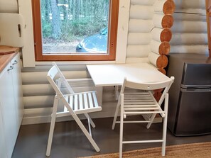 A compact kitchen with a window view of a forest and road, a white table with two chairs, and a black refrigerator.