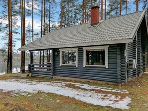 Une cabane en rondins avec un toit en métal, une cheminée et une véranda dotée d’une balustrade.