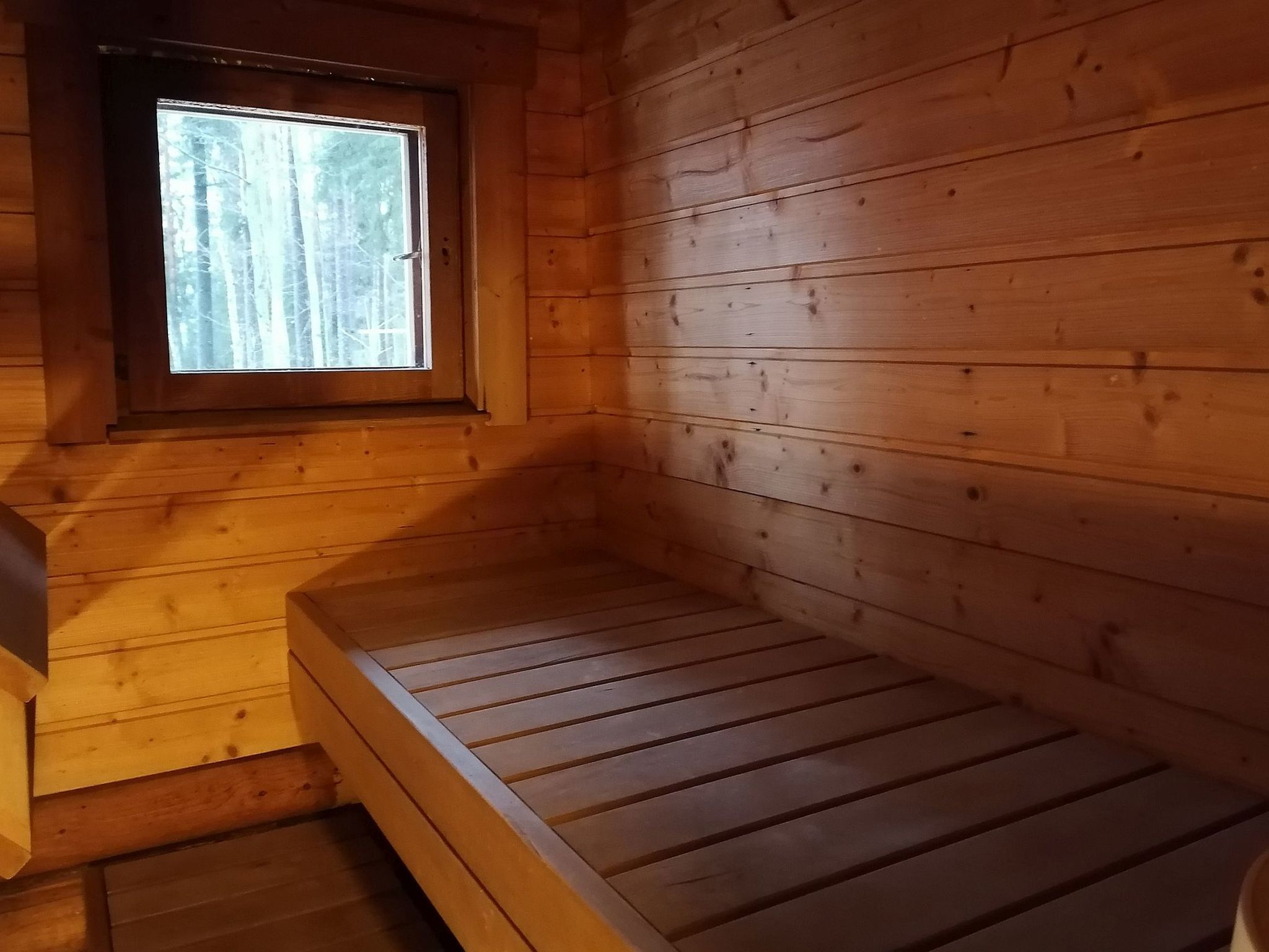 Une pièce de cabane en bois avec un lit simple, une fenêtre et un plancher en bois.