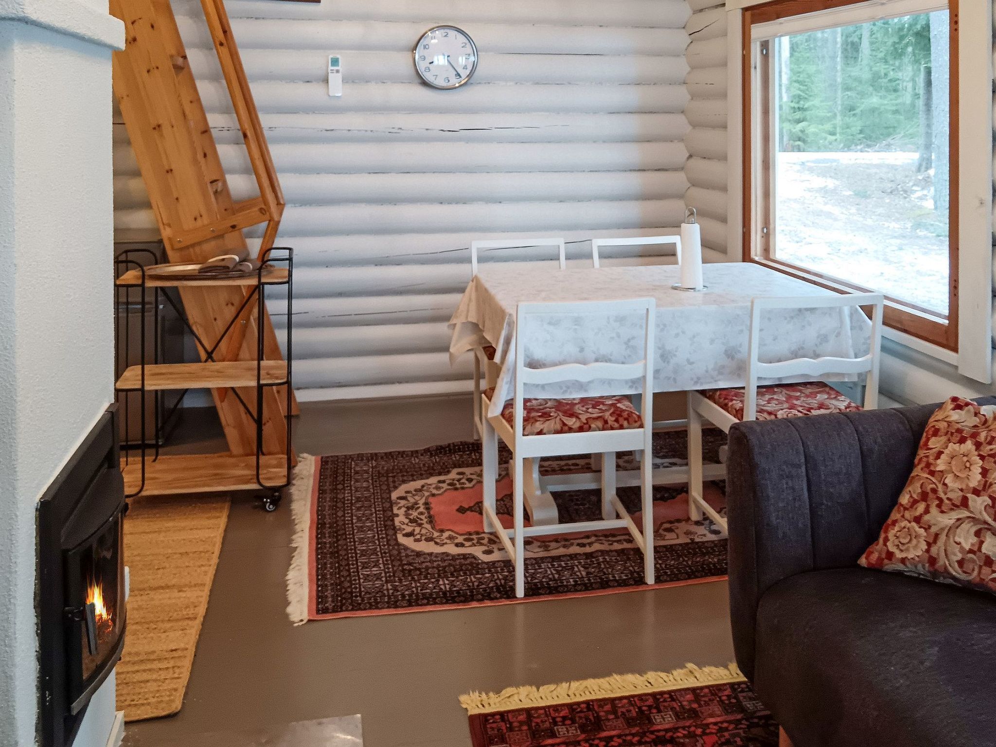 A cozy cabin interior with a fireplace, a dining table with chairs, a sofa, and a window with a view of the outdoors.