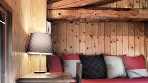 Ein Holzblockhaus-Innenraum mit einem Holztisch, einem Stuhl und einer Bank mit Kissen.