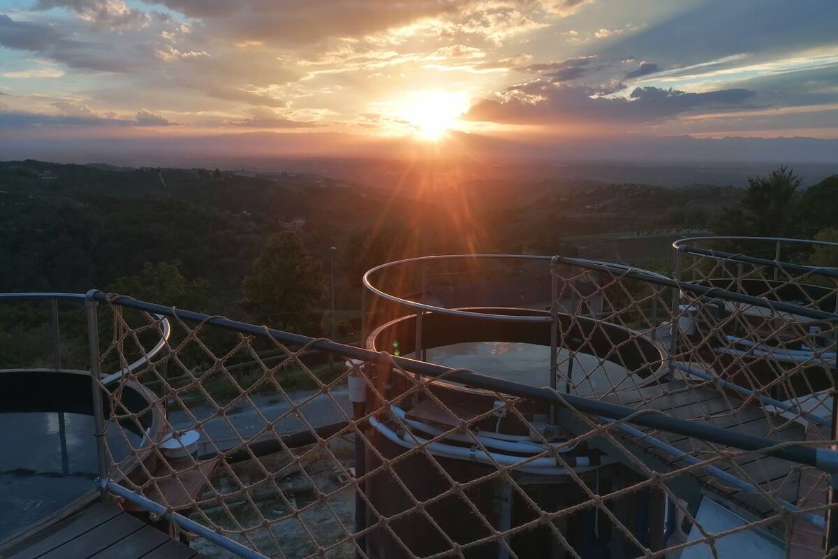 Vista de un atardecer sobre un paisaje montañoso, con una valla metálica y una estructura circular al frente.