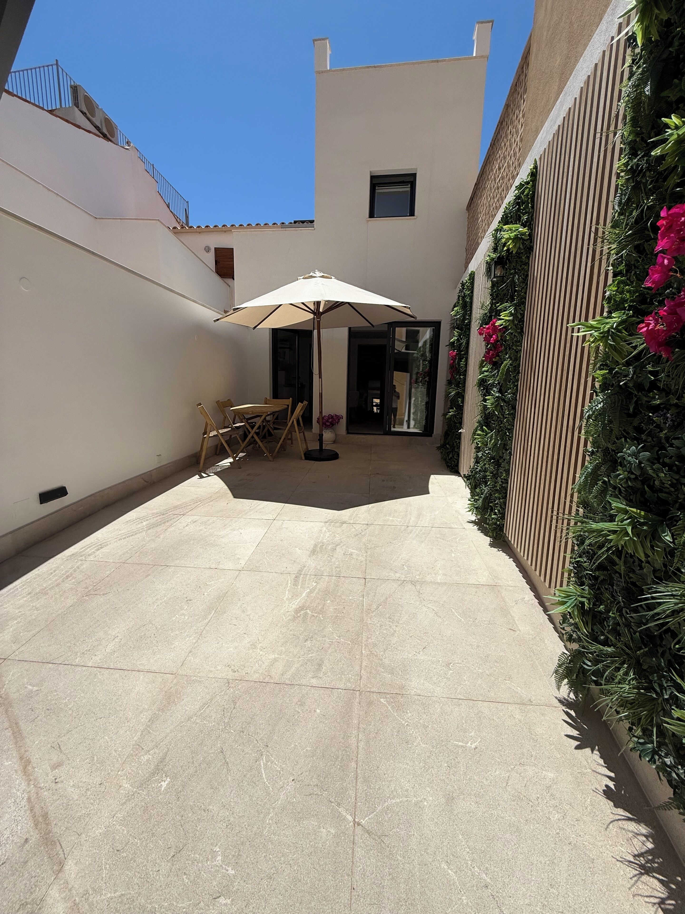 Un espace patio aménagé avec une table et des chaises, un grand parasol et un mur recouvert de plantes grimpantes.