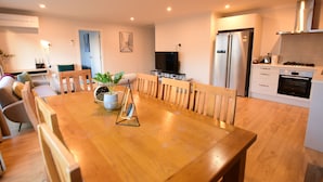 A modern kitchen with a built-in oven, a refrigerator, and a dining area with a wooden table and chairs. - Alpine Star - 3 Bedrooms B (Lake Tekapo)