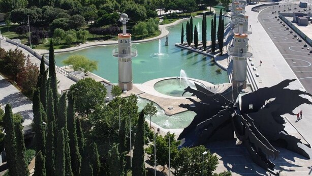 Ein Park mit Springbrunnen, einer großen Skulptur und hohen Bäumen.