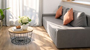 Ein modernes Wohnzimmer mit einem grauen Sofa, einem runden Couchtisch und einem Fenster mit Vorhängen.