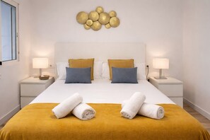 Hotellihuone, jossa on sänky, kaksi yöpöytää, kaksi lamppua, seinätaideteos ja kaksi pyyhettä sängyllä.
