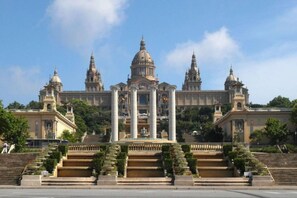 A grand building with a central dome, flanked by smaller domes, and a staircase leading up to the entrance. - APARTMENTS BCN CENTRAL-ATICO SANTS (Barcelona)