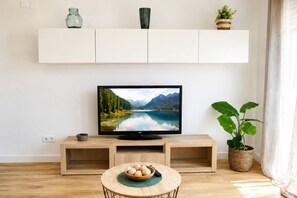 Un soggiorno con televisore, mobile TV in legno, un tavolino rotondo con una ciotola di frutta e una pianta in vaso.