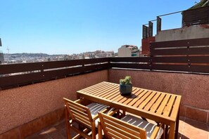A rooftop terrace with a wooden table and chairs, a potted plant, and a view of the cityscape. - APARTMENTS BCN CENTRAL-ATICO SANTS (Barcelona)