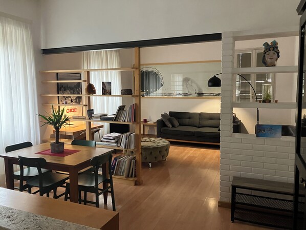 A modern living room with a sofa, a dining table with chairs, and a bookshelf filled with books and decorative items.