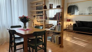 A cozy living room with a wooden dining table, two chairs, a bookshelf, and a black sofa. - Monti Parioli House (Roma)