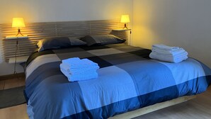 A neatly made bed with a blue and black checkered bedspread, two bedside lamps, and folded towels on the bed. - Monti Parioli House (Roma)