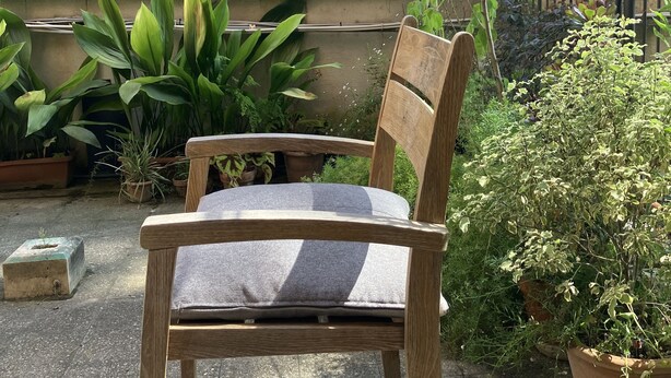 A wooden chair with a cushion in a garden area with potted plants and a building in the background. - Monti Parioli House (Roma)